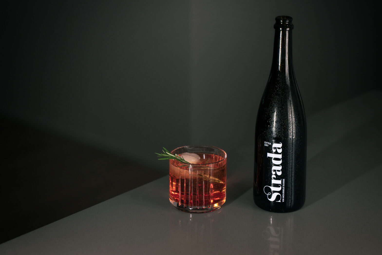 Der Sekt Cocktail Strada Roseberry mit einer Flasche Strada Extra Dry auf einer Ablage